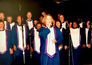 Mary singing solo on stage, on microphone with the Oakland Interfaith Gospel Choir