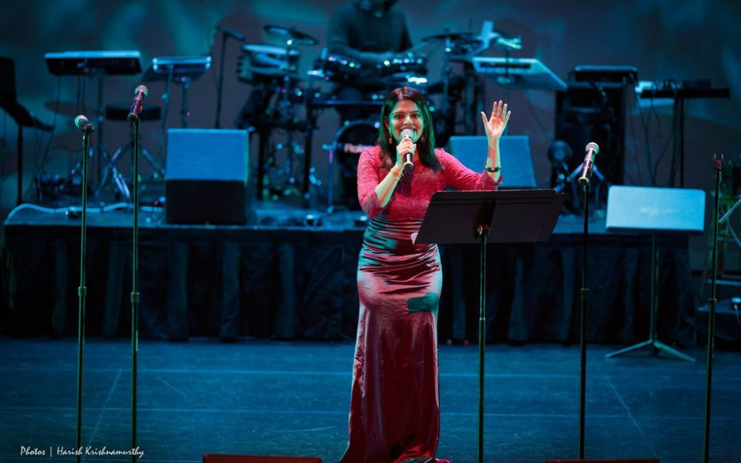 Vidya on stage in a red dress singing with a microphone in her hand