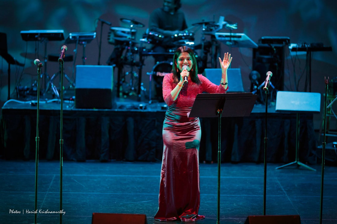 Vidya on stage in a red dress singing with a microphone in her hand
