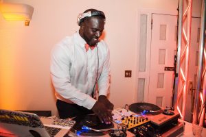 Justin James at his turntable playing in an orange bowtie an white shirt.