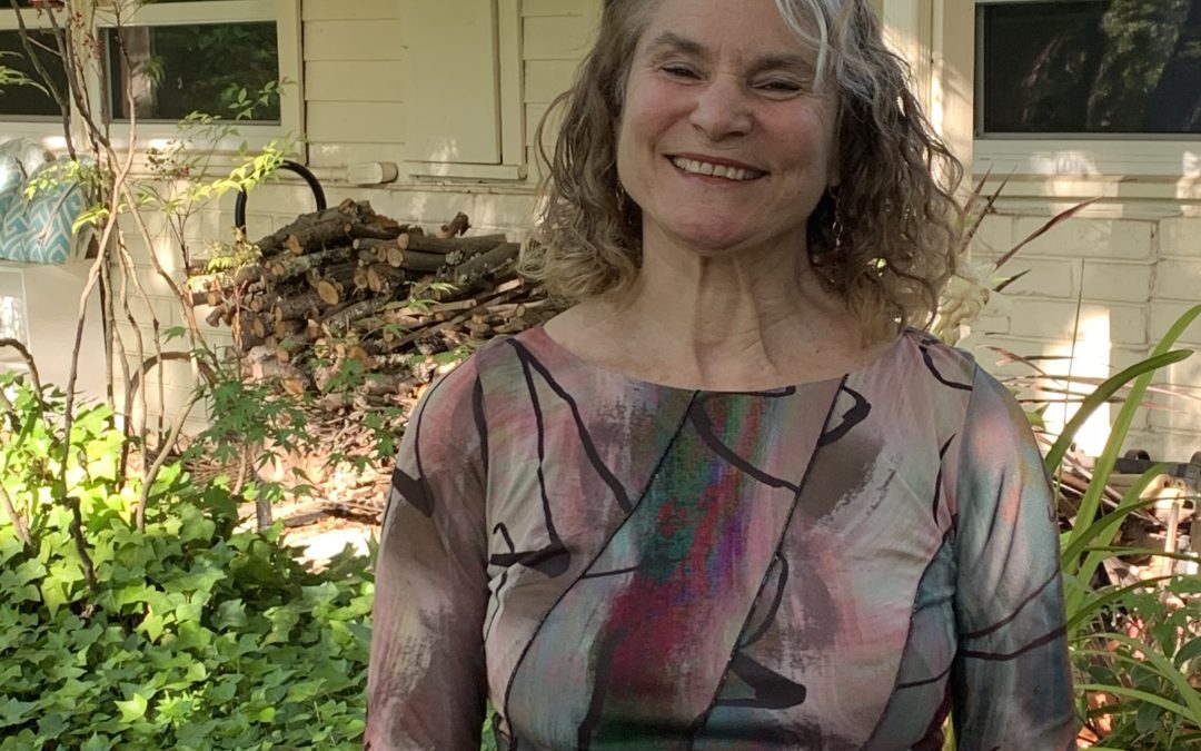 Picture of Betsy Blakeslee, woman with grey hair smiling in front of a house