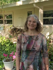 Picture of Betsy Blakeslee, woman with grey hair smiling in front of a house