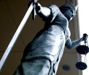 Statue of woman with sword resting on the ground holding scales and wearing a crown. Image by: Lady Justice by Leonard Matthews. Creative commons license.
