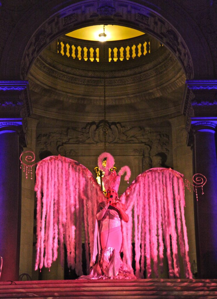 woman dressed in pink wearing giant pink wings standing in a building rotunda