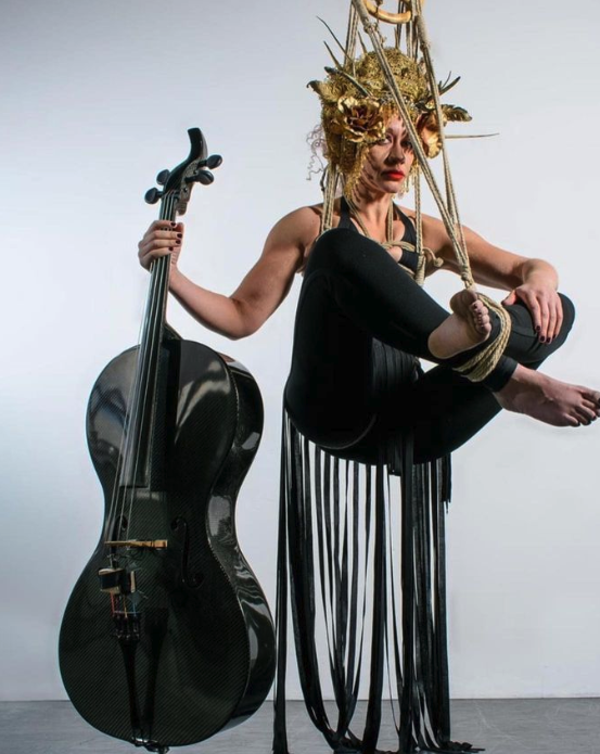 Woman suspended in the air wearing a black leotard holding a black cello