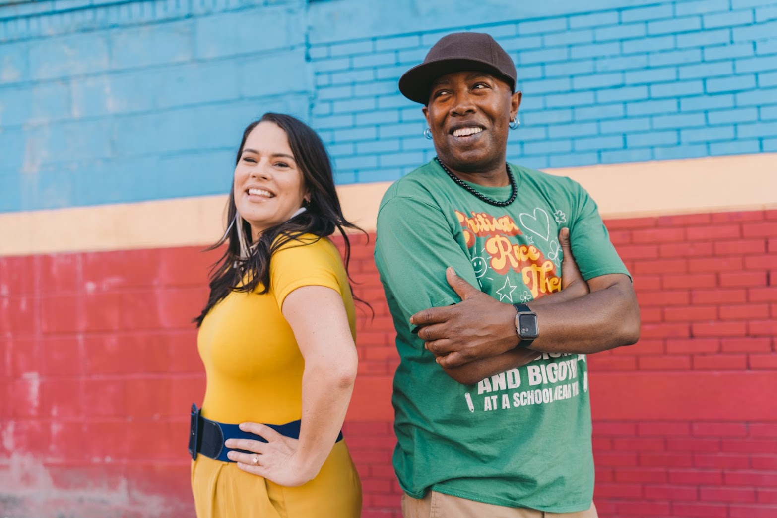 Woman in yellow and man in green against a red white a blue wall smiling