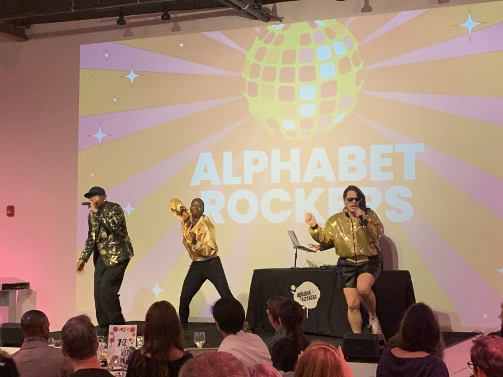 Alphabet Rockers Tommy, Kaitlin, and Samara Atkins performing on stage in 2023.