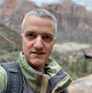 Man in a parka facing camera with desert mountains in background