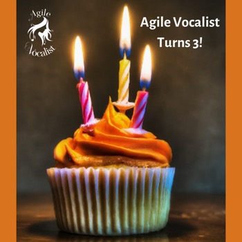 Orange frosted cupcak with 3 lit candles on it. Text: Agile Vocalist turns 3!