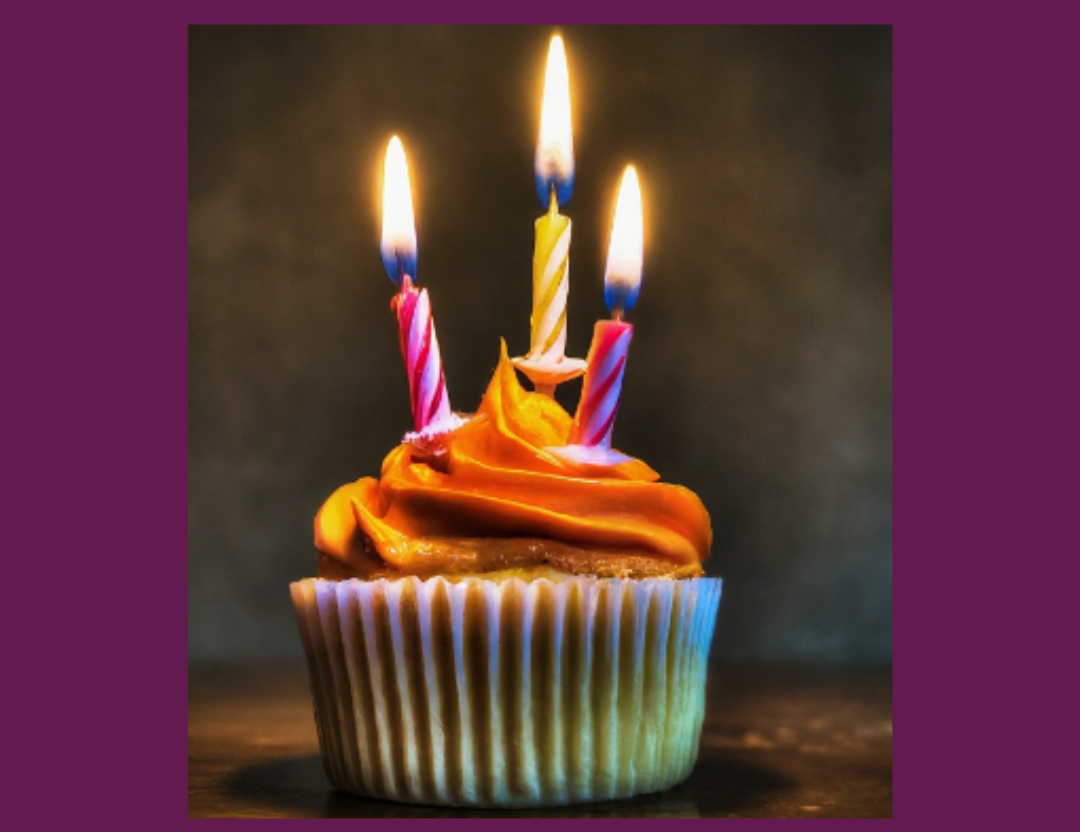 cupcake in colorful wrapper with 3 lit candles on it