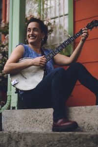 Woman seated on stairs holding a banjo, smiling and looking off to the side.