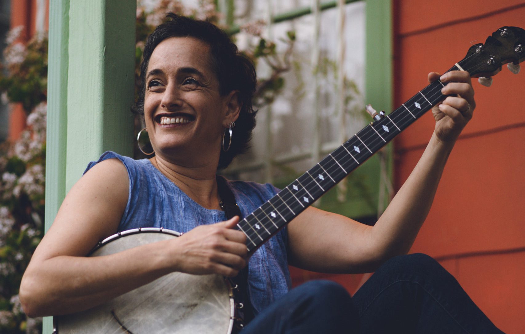 Woman seated on stairs holding a banjo, smiling and looking off to the side.